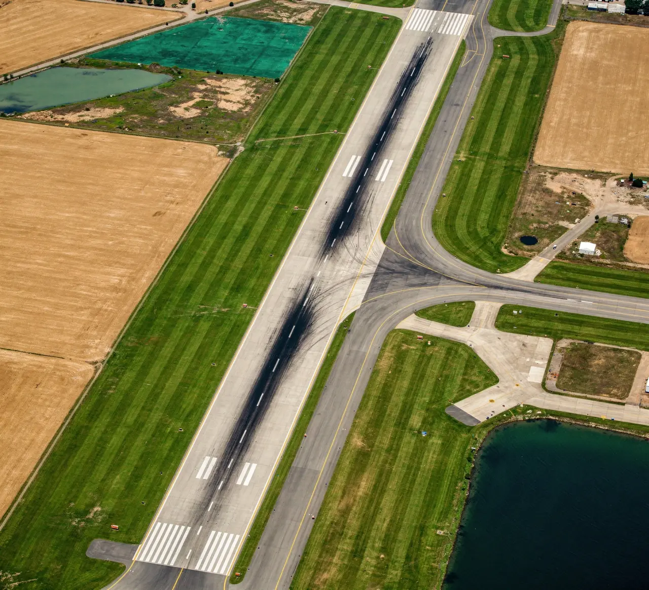 An overhead view of an airport runway and taxiways surrounded by grass and fields